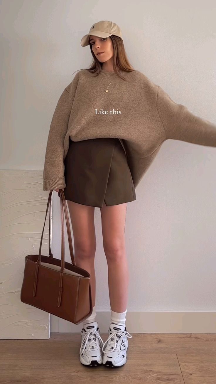 Woman in a baseball cap, oversized sweater, and mini skirt holding a tote bag