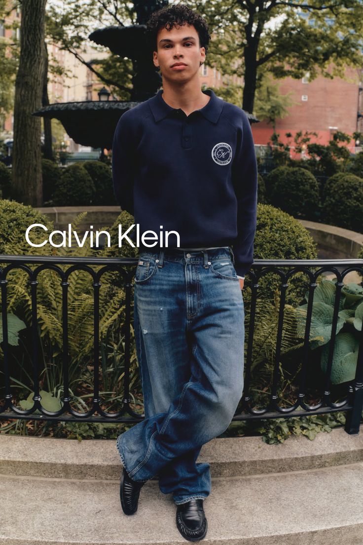 Man with curly hair wearing a navy polo shirt and loose jeans in an urban park
