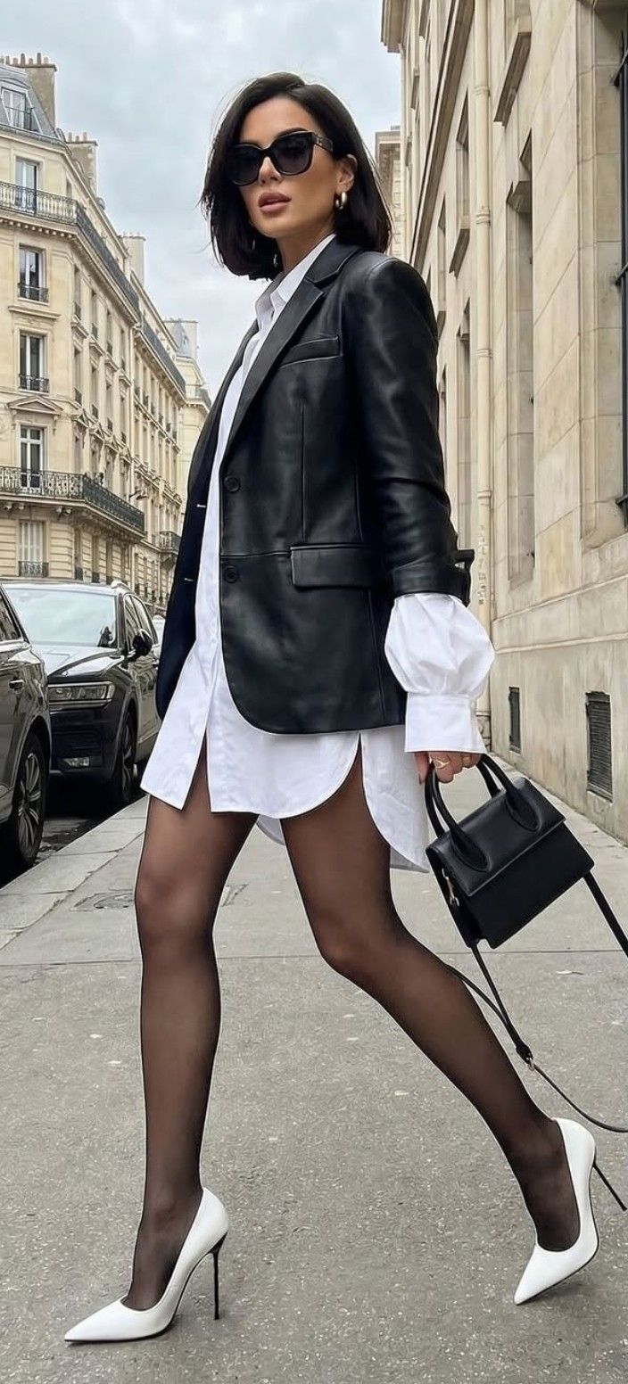 Woman in a leather jacket and white shirt dress walking on a city street