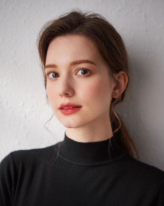 Woman in a black turtleneck with a ponytail and red lipstick looking at the camera