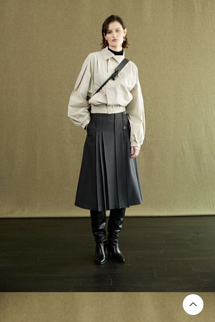 Woman in a beige jacket and pleated skirt with a crossbody bag