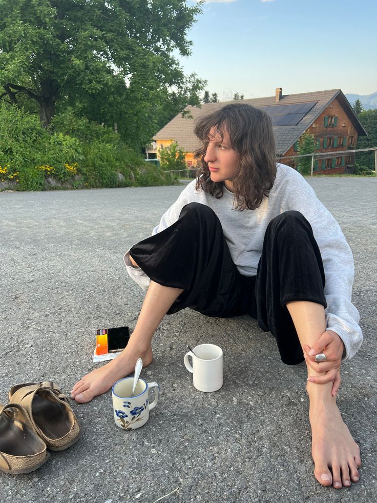 Person with long hair sitting barefoot on the ground outdoors