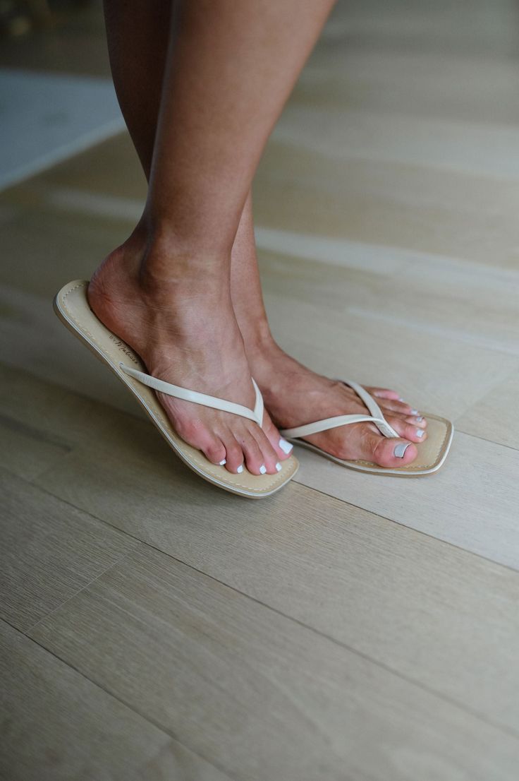 Person wearing white flip flops with white nail polish on a light wood floor