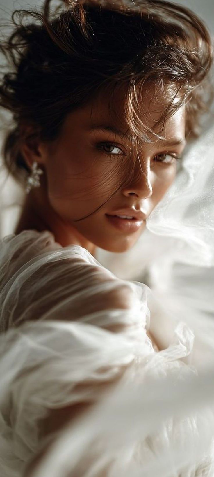 Woman with dark hair and sheer fabric looking over her shoulder