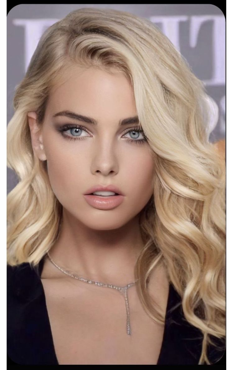 Blonde woman with blue eyes and a necklace, looking directly at the viewer