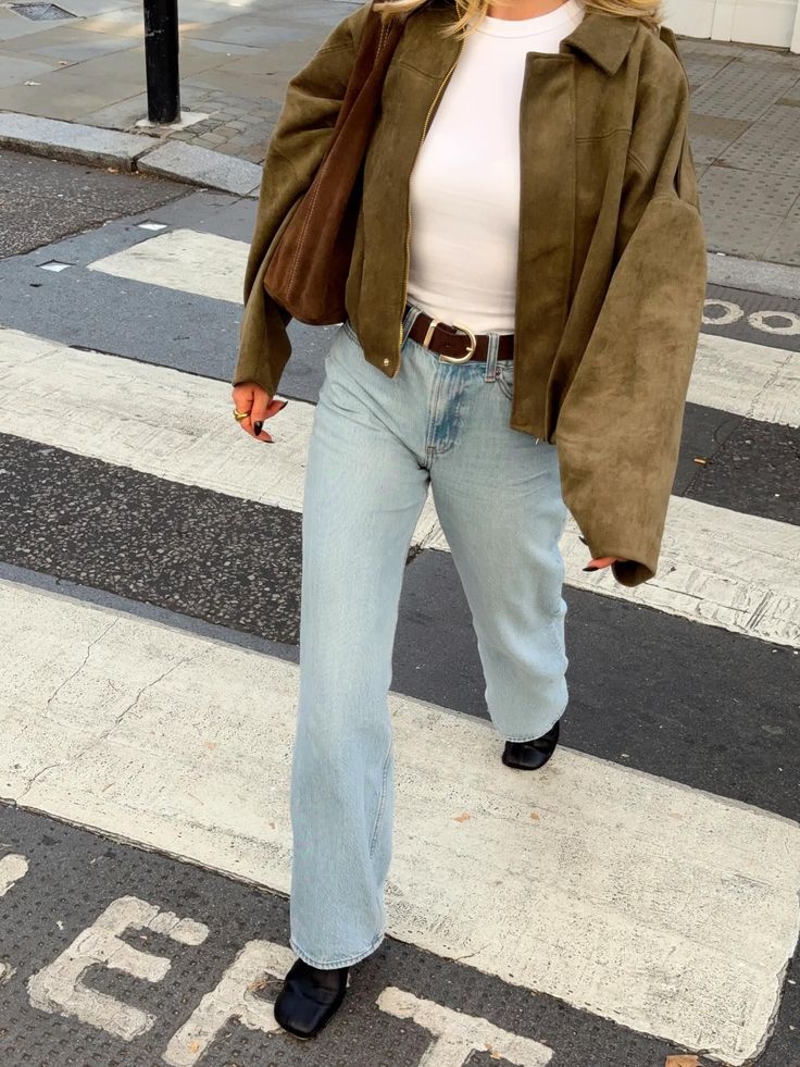 Person in a suede jacket and light wash jeans walking on a crosswalk