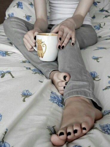 Person holding a cat mug while sitting on a bed with floral sheets