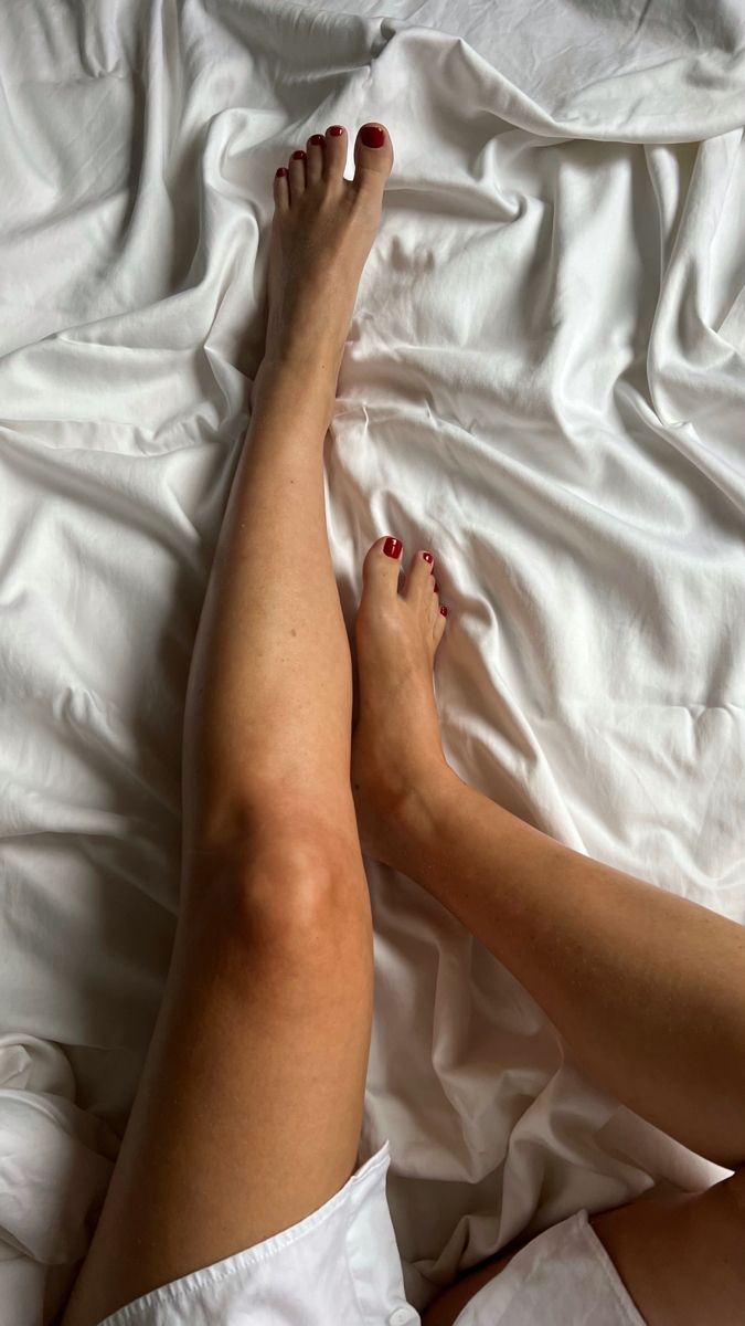 Person's legs with red nail polish on white bed sheets
