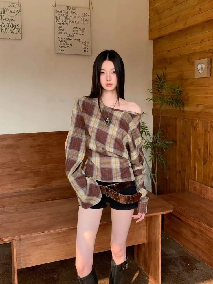 Woman with long black hair wearing a plaid shirt and black shorts indoors