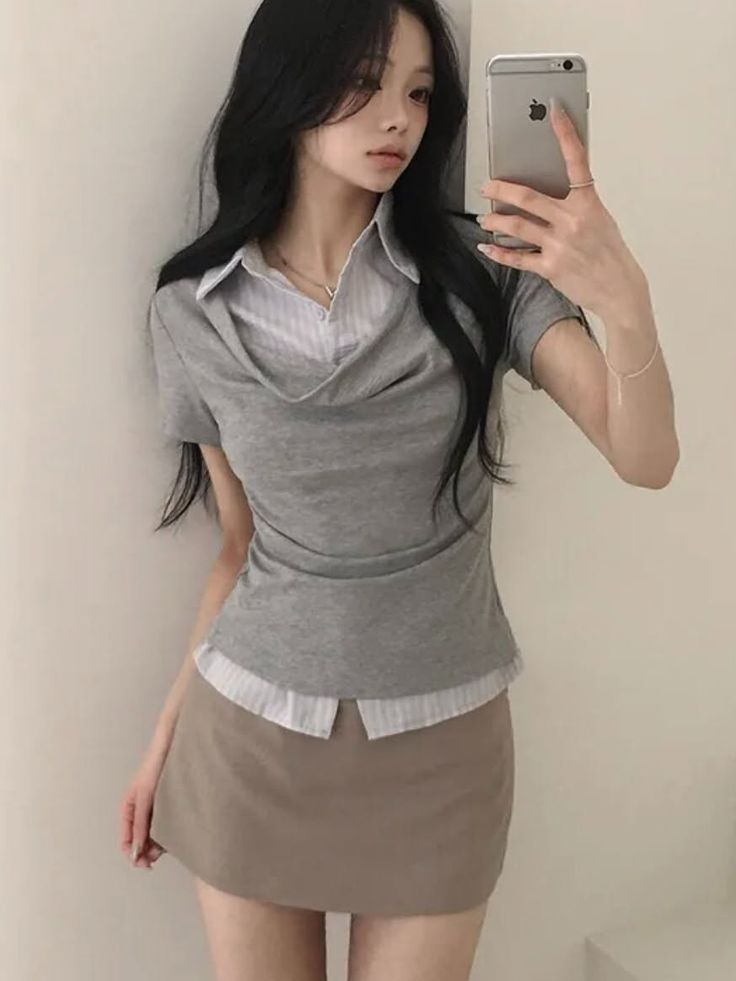 Woman with long black hair taking a mirror selfie in a grey top and mini skirt