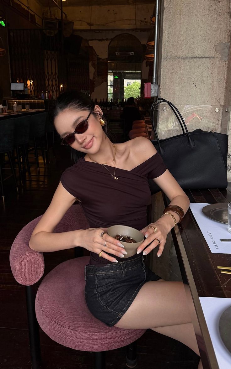 Woman in an off-shoulder top and denim skirt holding a bowl in a restaurant