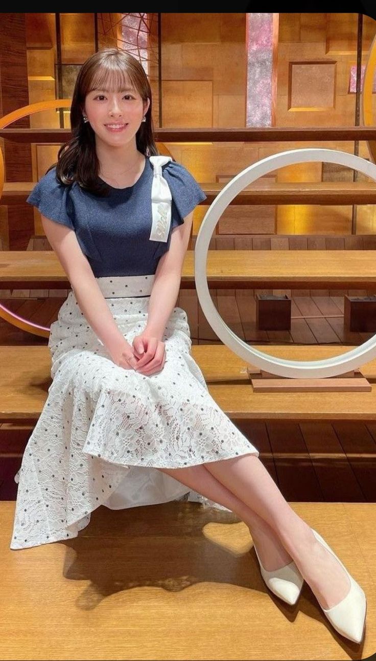 Woman with long hair wearing a blue top and white skirt, sitting indoors