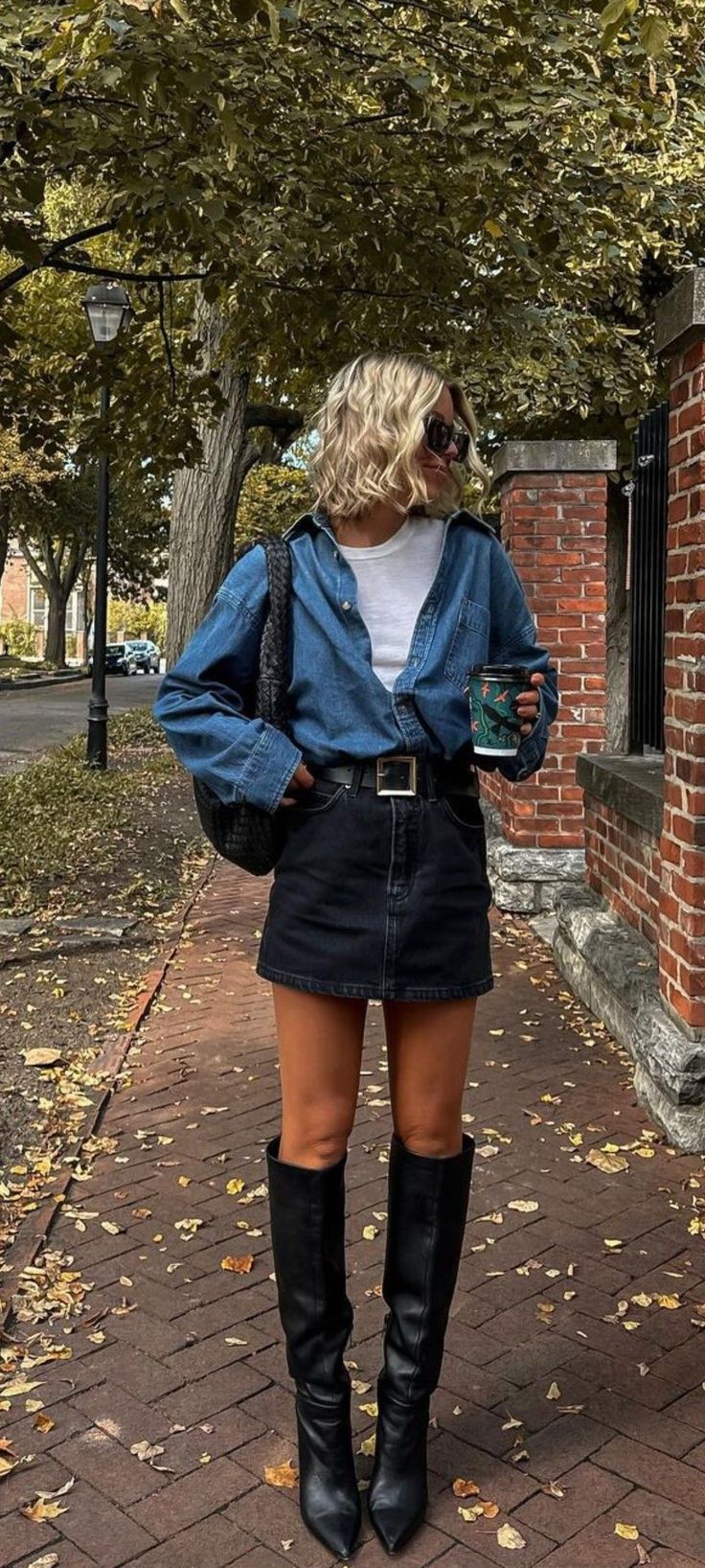 Woman in a denim shirt and black mini skirt walking on a street with autumn leaves