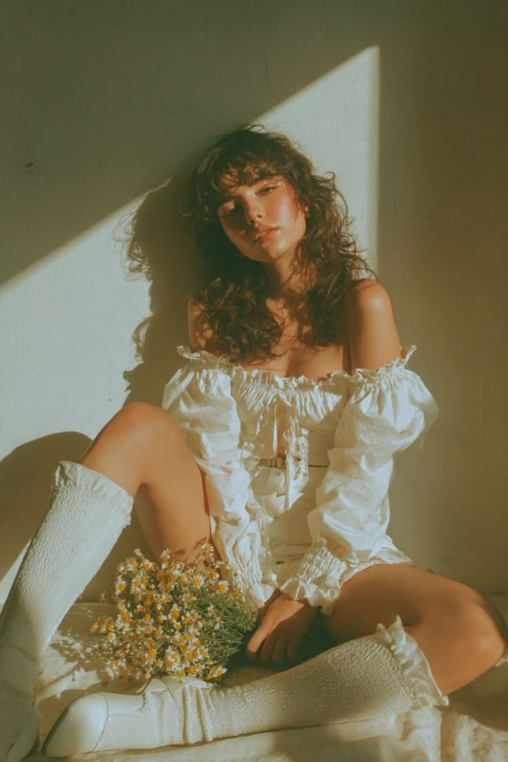 Woman with curly hair in an off-shoulder top holding a bouquet indoors