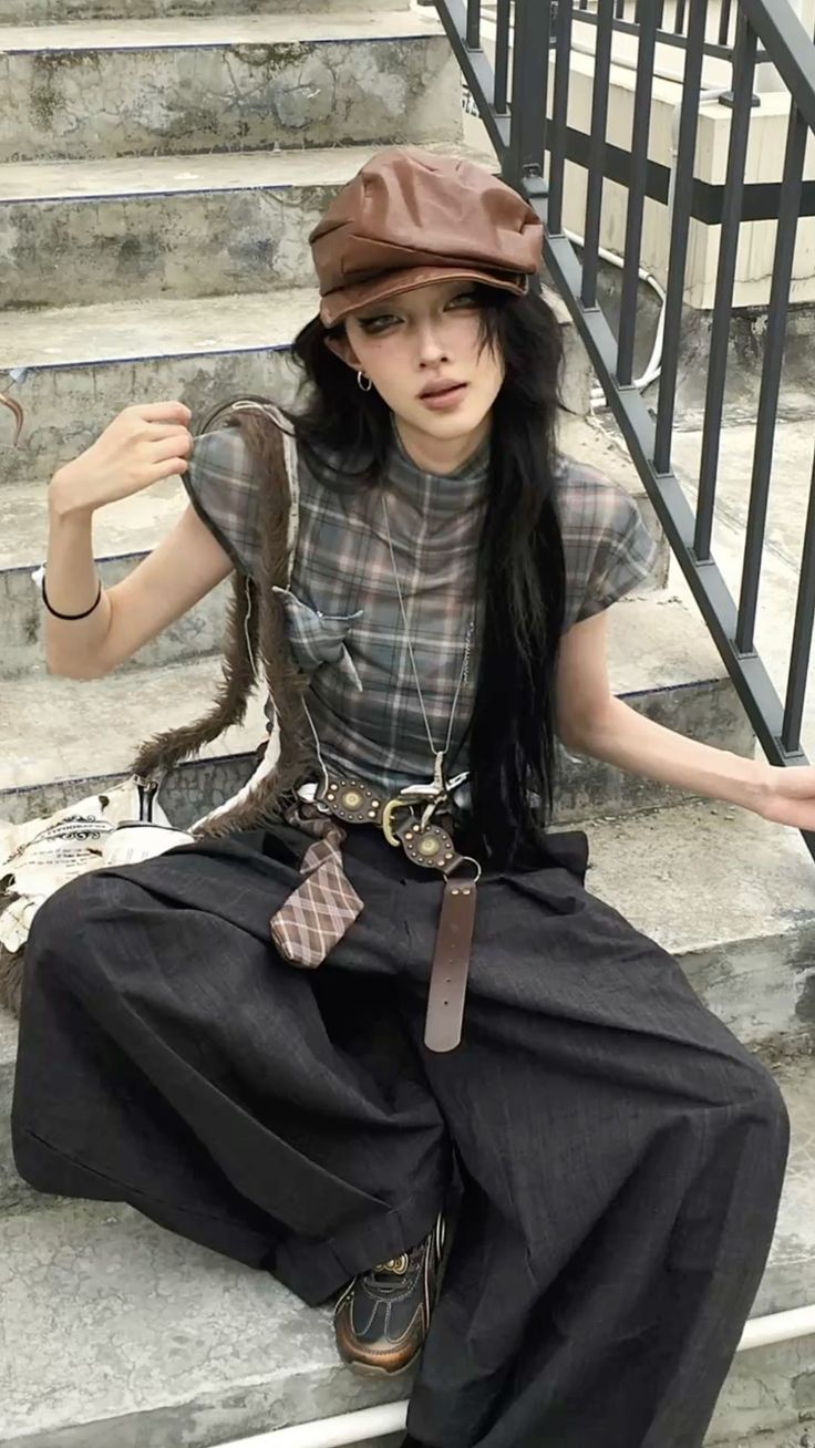 Person with long black hair and a brown hat sitting on concrete stairs
