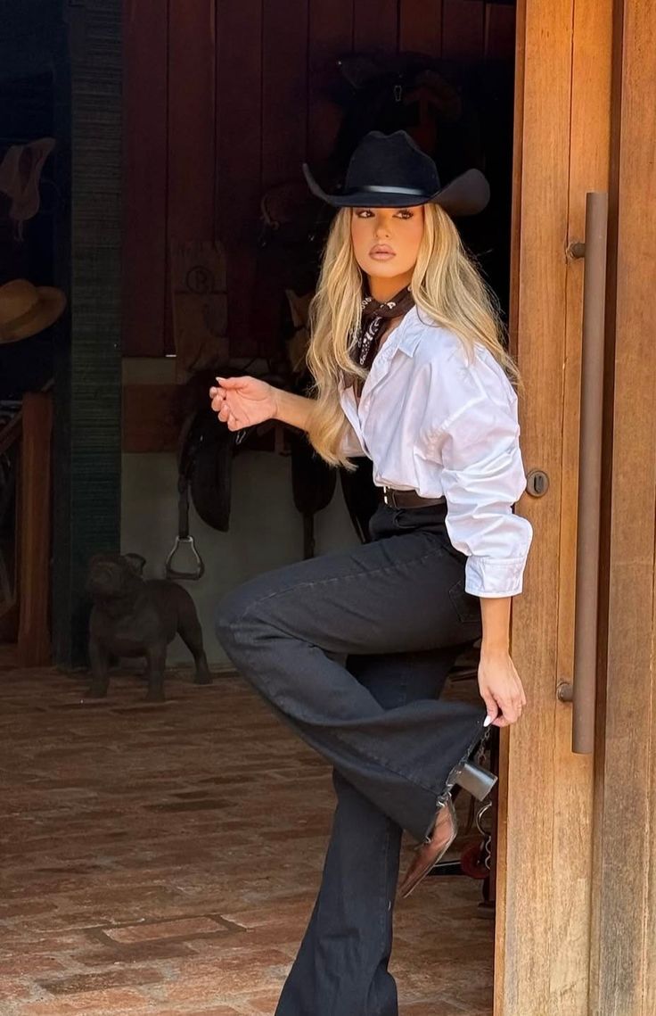 Woman in a cowboy hat and white shirt posing indoors with a dog in the background