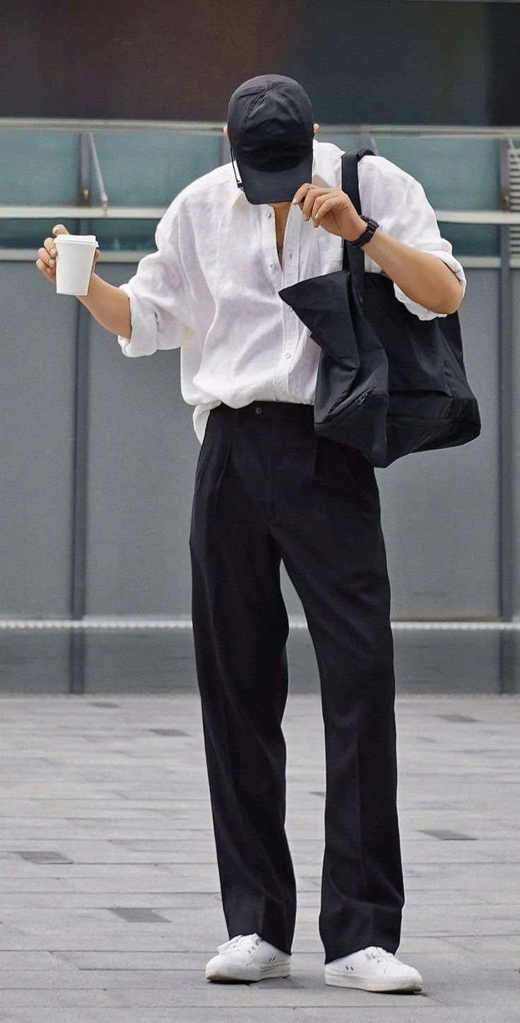 Person in a white shirt, black pants, and baseball cap holding a coffee cup