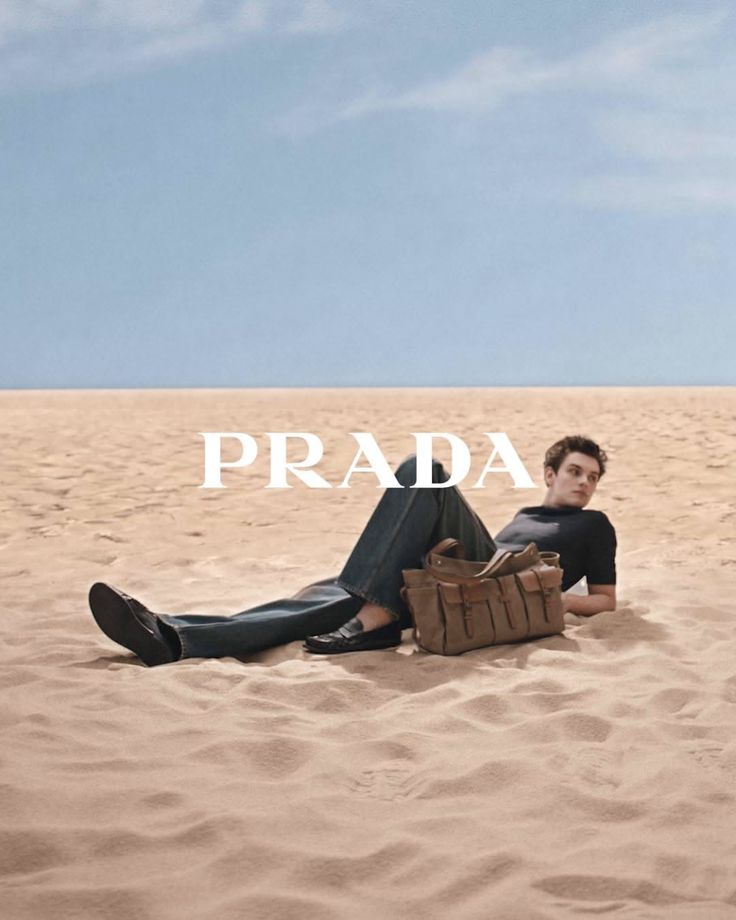 Man in jeans and a black shirt lying on sand with a brown bag