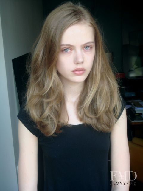 Young woman with long blonde hair and blue eyes wearing a black t-shirt indoors