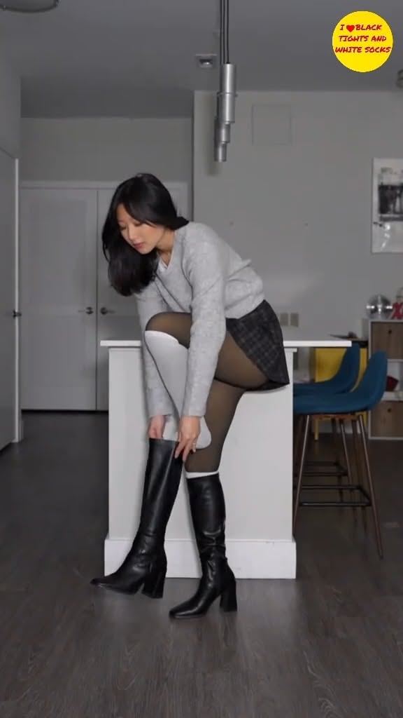 Woman in a plaid skirt and black boots adjusting her tights indoors