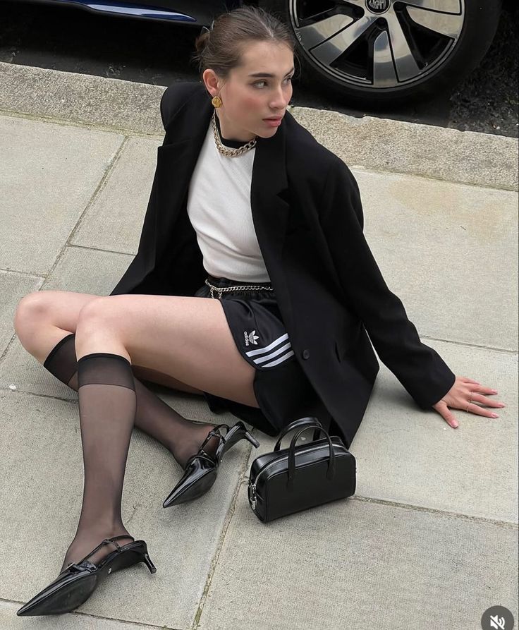 Woman in a black blazer and shorts sitting on the ground with a small handbag