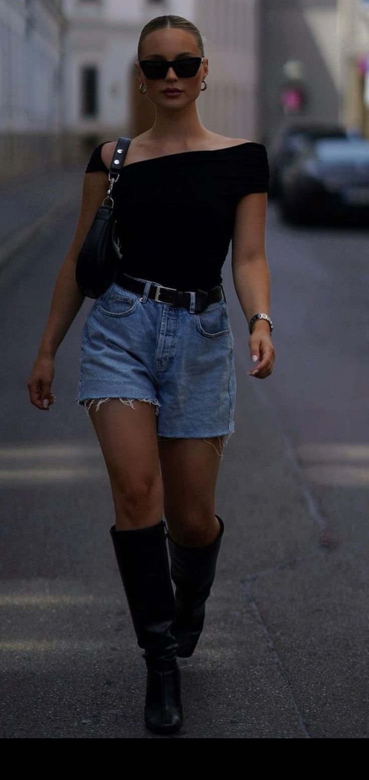Woman in denim shorts, black top, and boots walking on a street