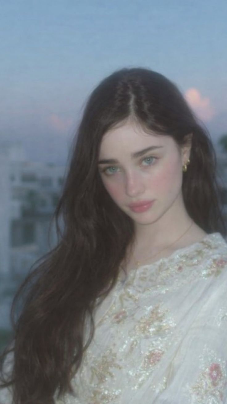 Woman with long dark hair and blue eyes wearing an embroidered top outdoors