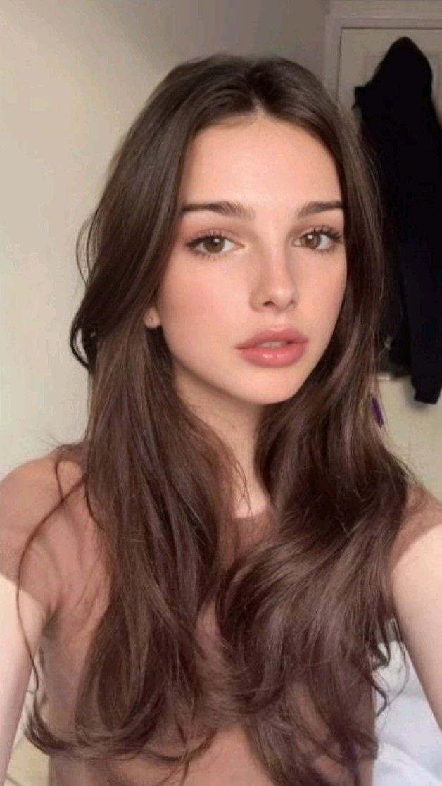 Young woman with long brown hair and natural makeup in an indoor setting