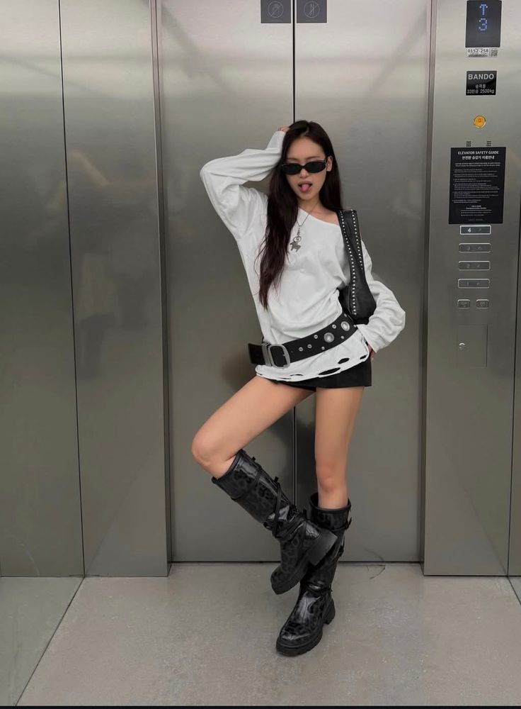 Woman in a white long sleeve and black shorts posing in front of an elevator