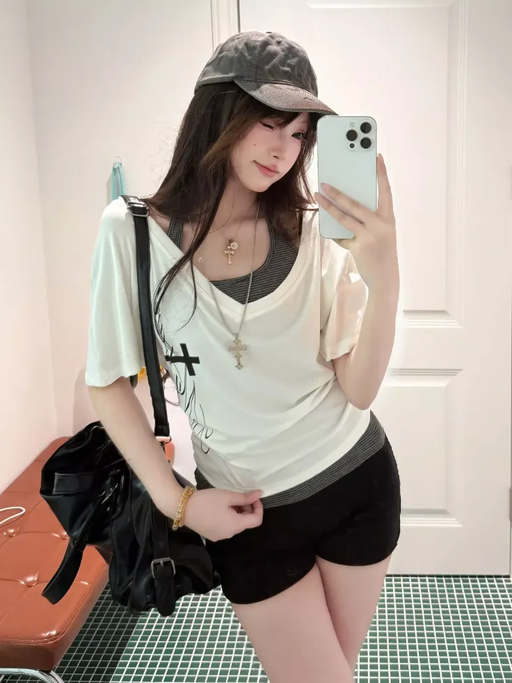 Woman in a baseball cap and t-shirt taking a mirror selfie indoors