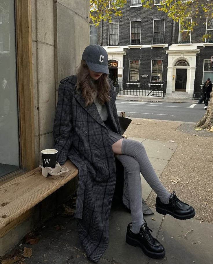 Woman in a plaid coat and baseball cap sitting on a bench outdoors