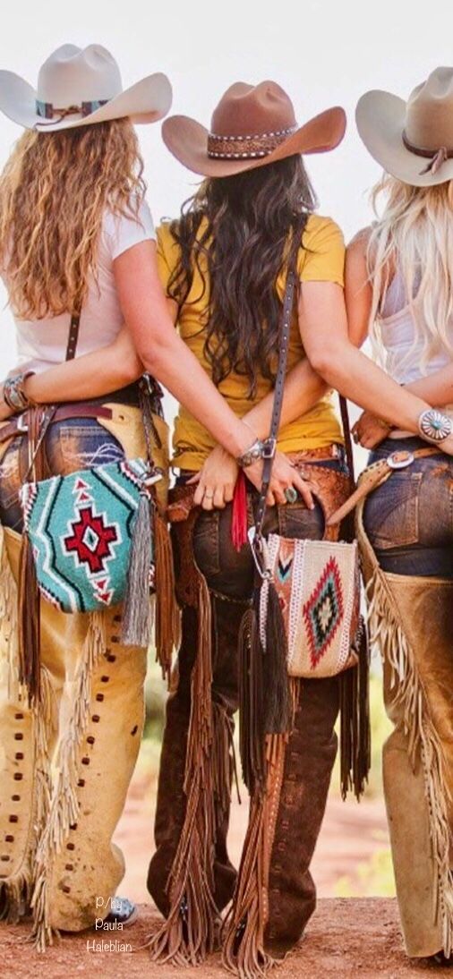 Three women in cowboy hats and chaps with their backs to the viewer