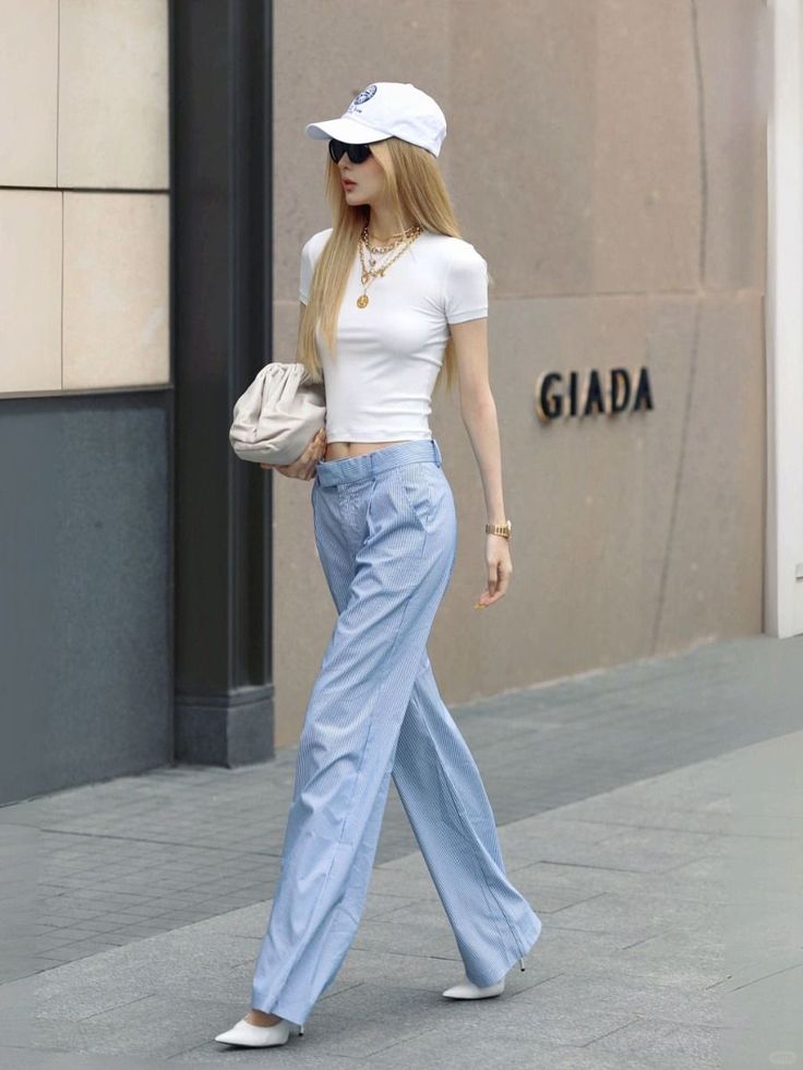 Woman with long blonde hair in a white crop top and striped pants walking outdoors
