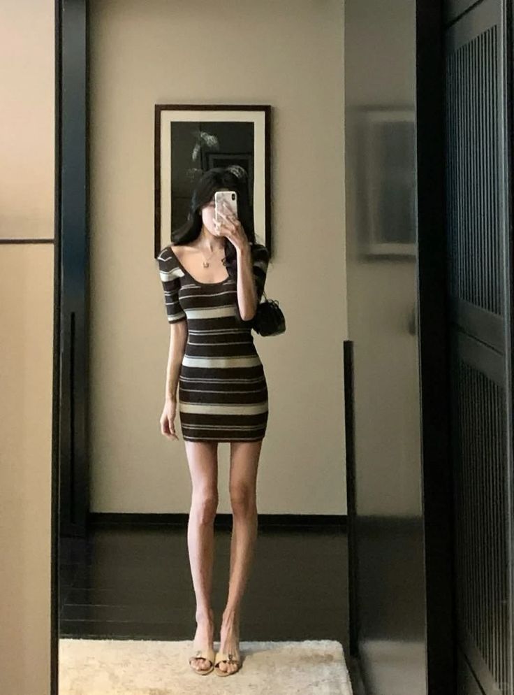 Woman in a striped dress taking a mirror selfie indoors