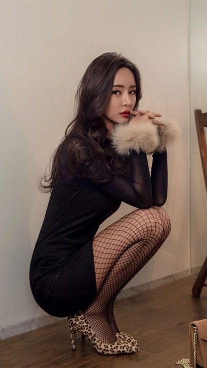 Woman in a black dress and fishnet stockings squatting indoors