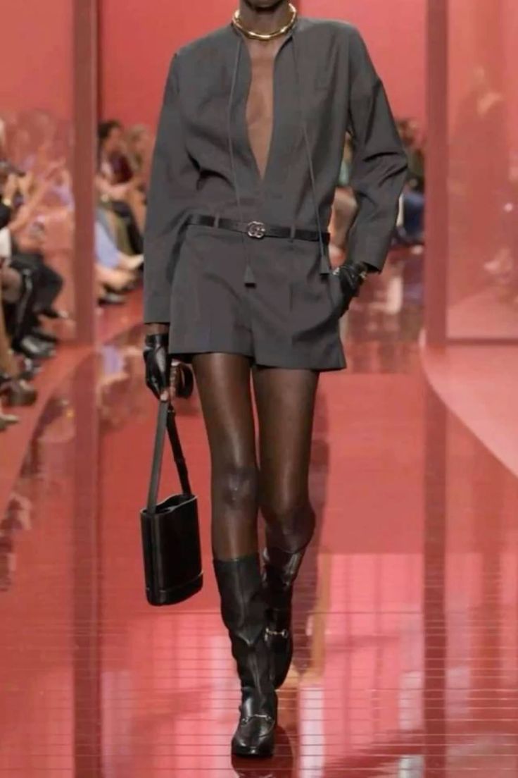 Model in a dark grey outfit with a deep V-neck on a red runway