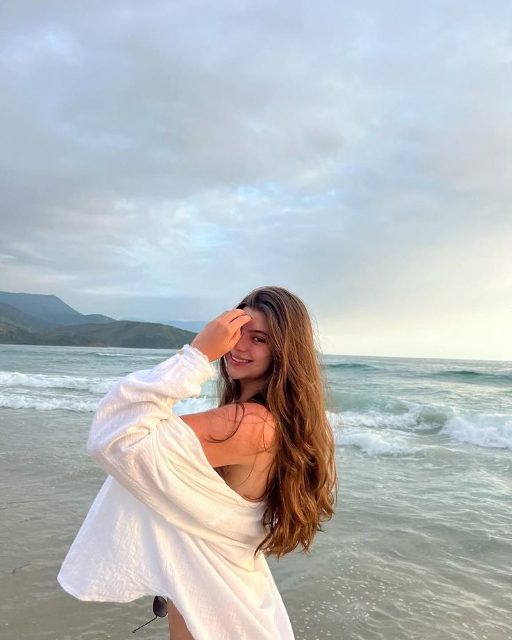 Woman with long hair on a beach, wearing a white shirt over a swimsuit