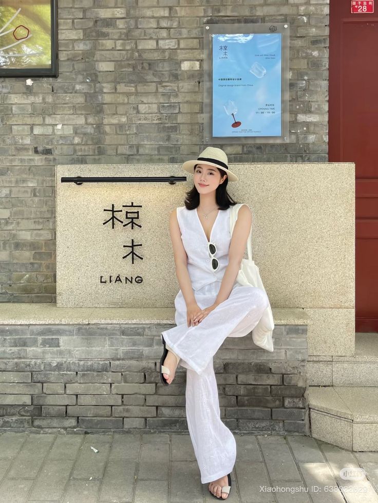 Woman in a white outfit and straw hat sitting outdoors