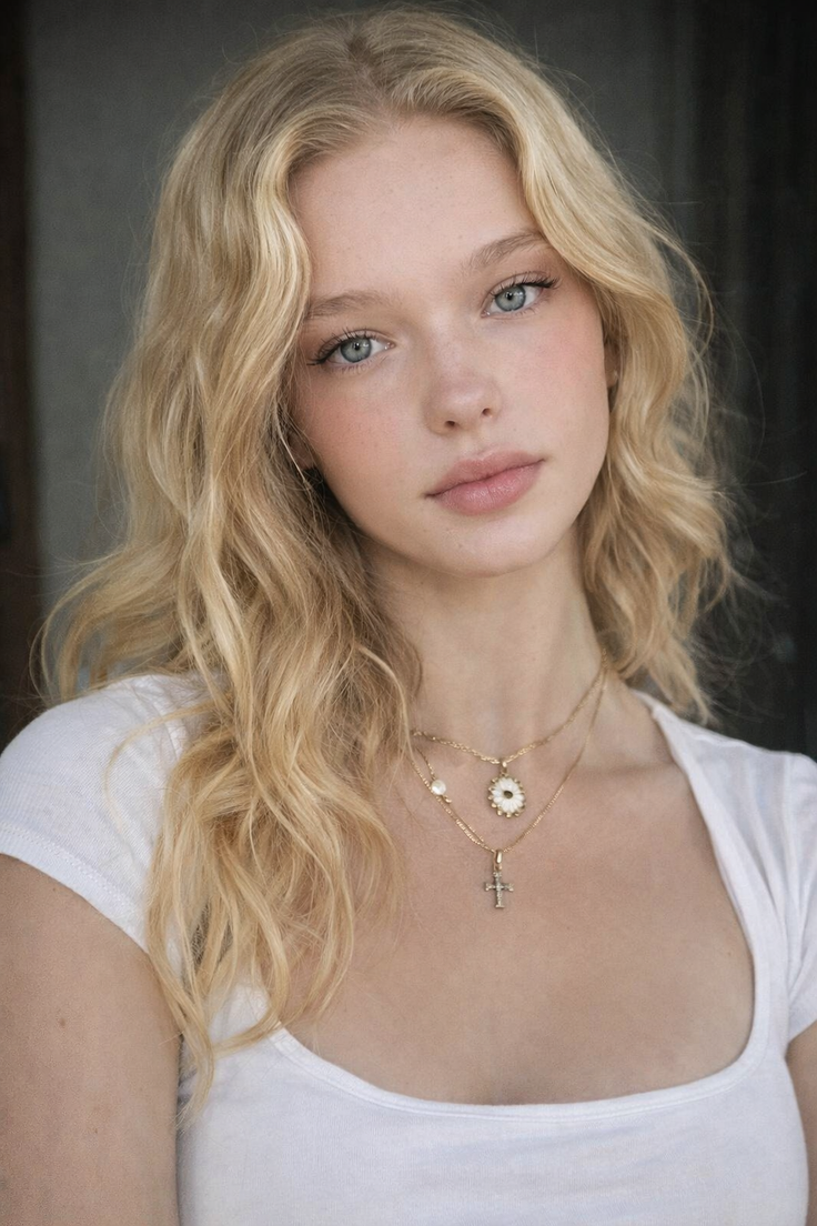 Young woman with blonde hair and blue eyes wearing a white shirt and necklaces