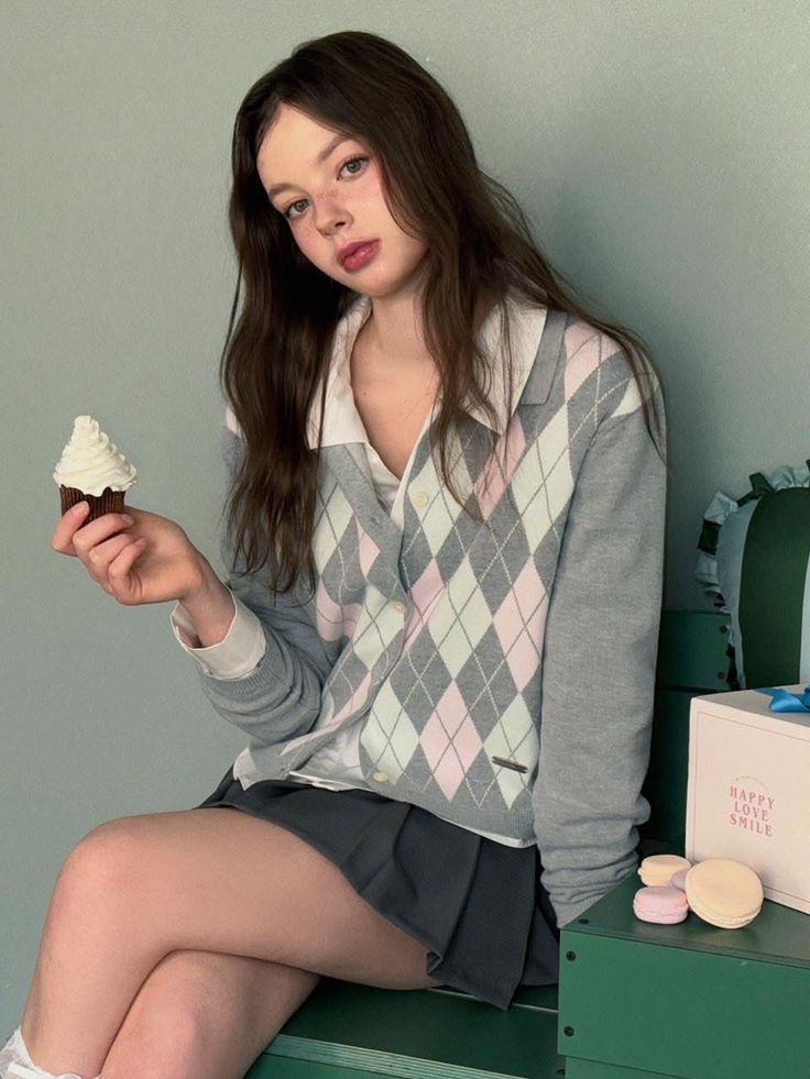 Young woman in an argyle cardigan holding a cupcake indoors