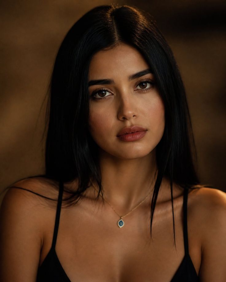 Woman with long black hair wearing a gold necklace with a blue charm