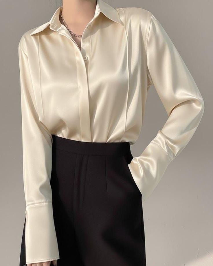 Person wearing a cream satin shirt and black pants with a silver necklace