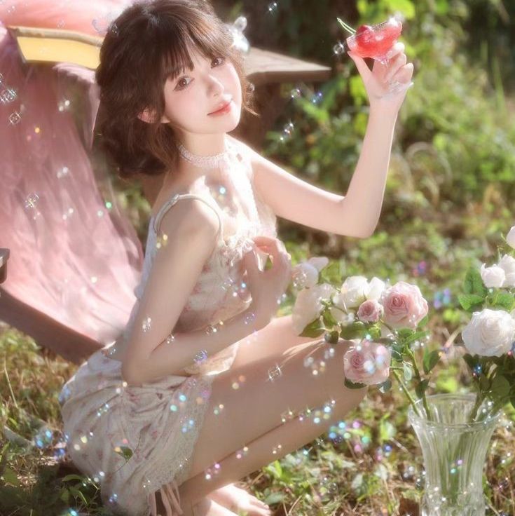 Woman in a floral dress holding a drink, surrounded by roses and bubbles outdoors