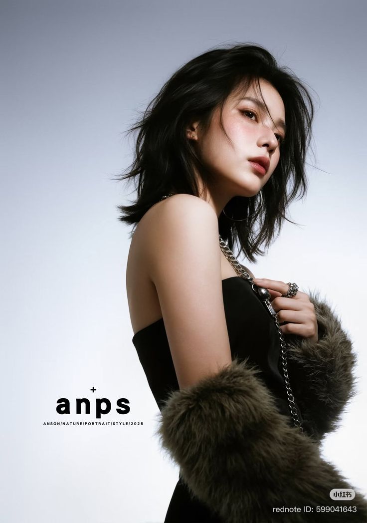 Woman with short black hair wearing a strapless top and fur sleeves, holding a silver chain