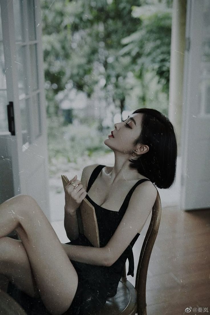 Woman in a black dress with short hair, holding a book indoors