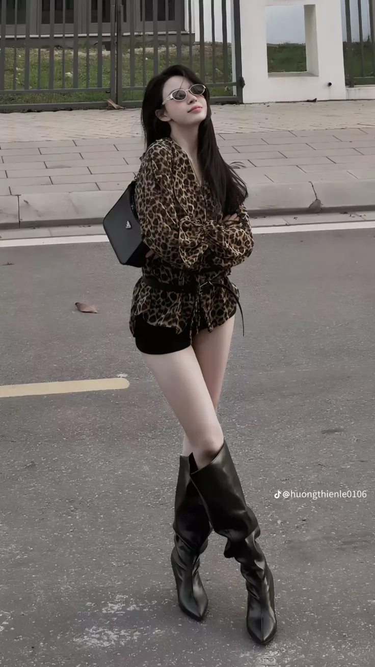 Woman in a leopard print shirt, black shorts, and tall boots on a street