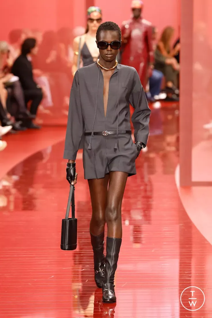 Model in a dark gray jumpsuit and knee-high boots on a red runway