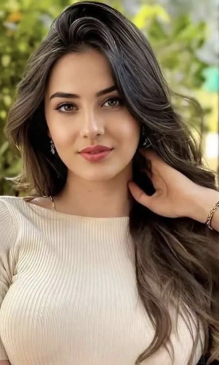 Woman with long brown hair wearing a ribbed top and jewelry outdoors
