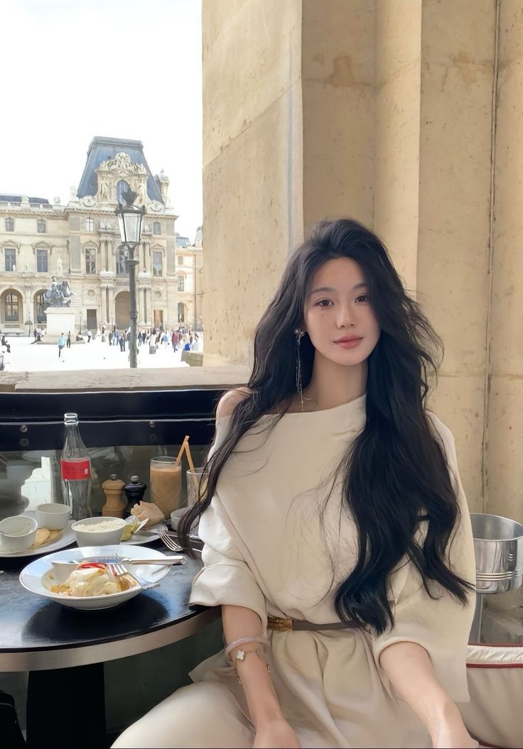 Woman with long dark hair at an outdoor cafe with a cityscape in the background