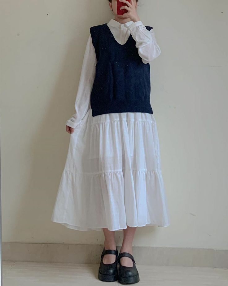 Person in a white dress and sleeveless sweater taking a mirror selfie